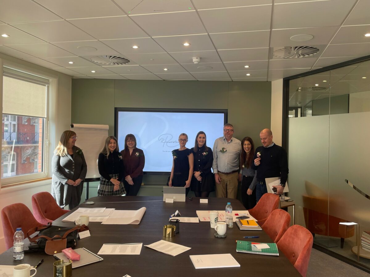 Some of the Riverstone team at the head office, they are stood in front of the presentation screen and behind a boardroom table.
