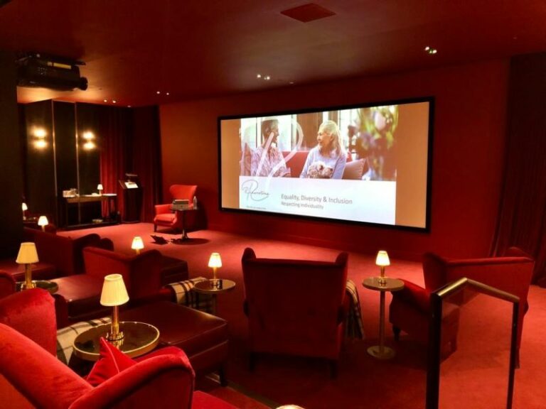 A luxurious cinema room, at the Riverstone Kensington residence, with individual arm chairs and tables facing a large screen with the words: "Riverstone. Equality, Diversity and Inclusion"