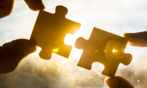Two puzzle pieces being put together, they are each being held by a hand.